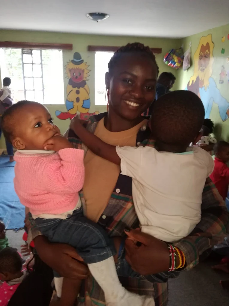 Caregiver holding two smiling children at Haven Kids Home